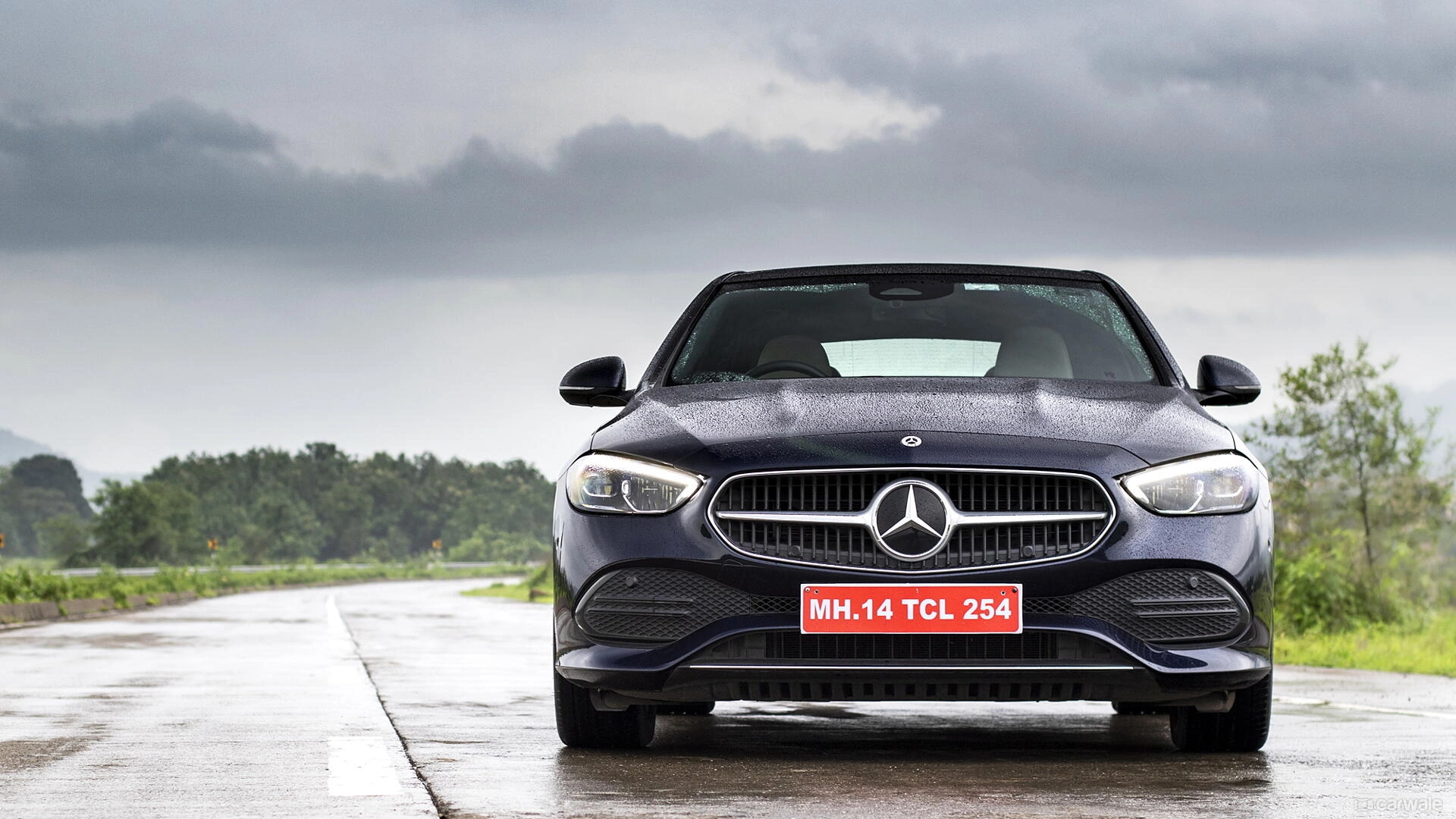 Black Mercedes-Benz C-Class luxury sedan front view on wet road with dramatic cloudy sky