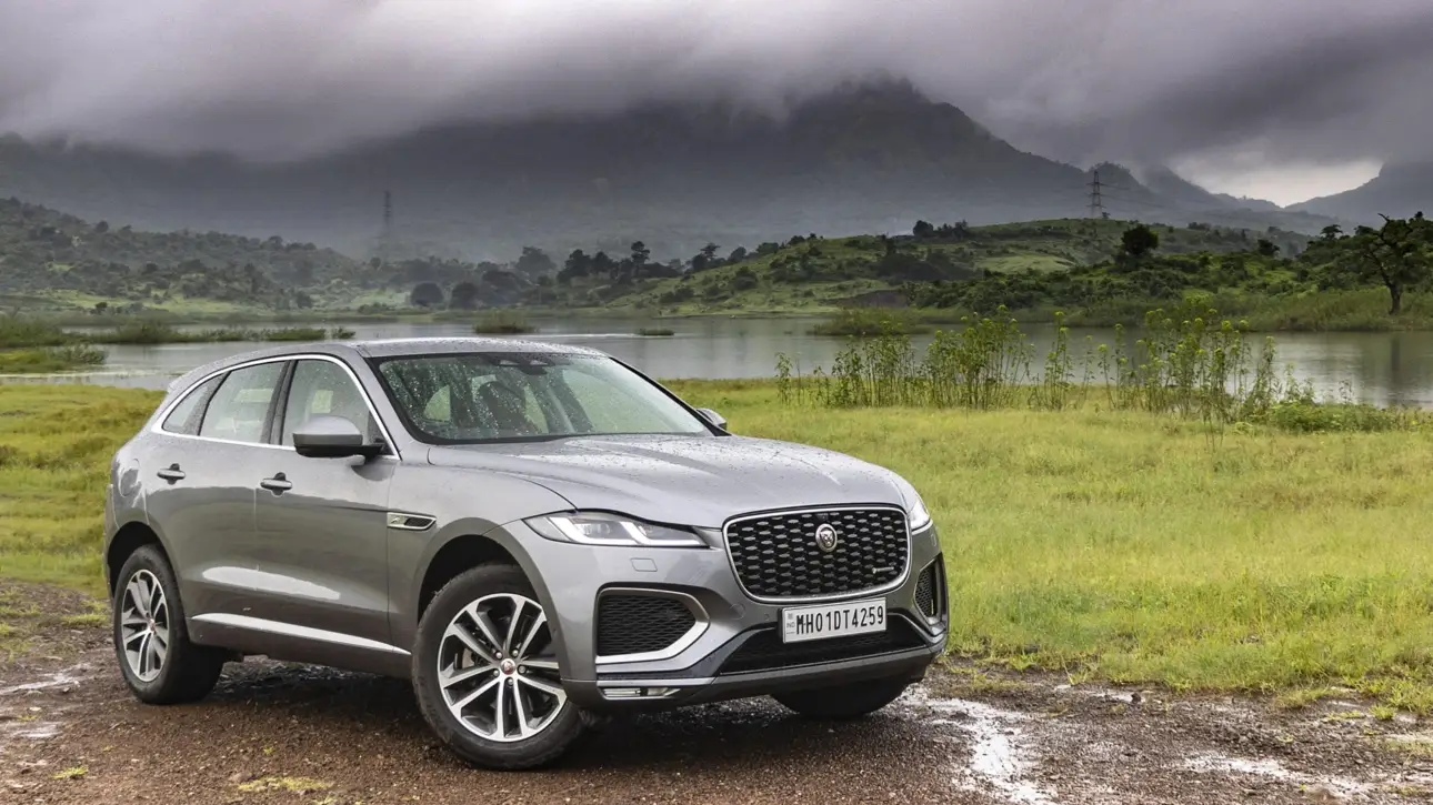Silver gray Jaguar F-PACE luxury SUV parked by lake with dramatic mountain landscape