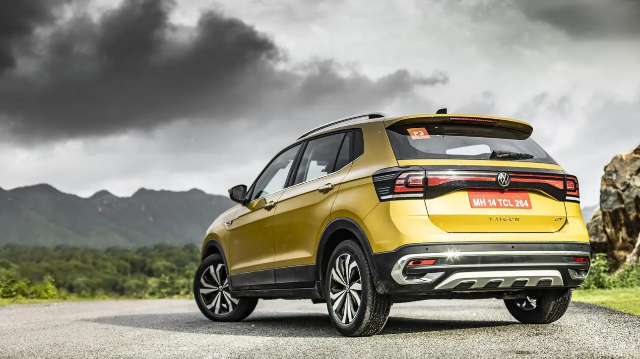 Yellow gold Volkswagen Taigun compact SUV rear three-quarter view with dramatic mountain landscape