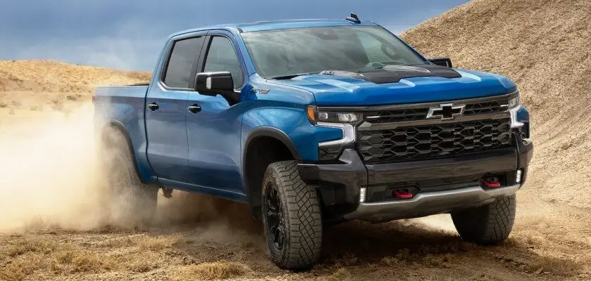 Blue Chevrolet Silverado off-road pickup truck driving through desert terrain kicking up dust