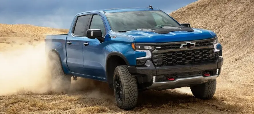 Blue Chevrolet Silverado off-road pickup truck driving through desert terrain kicking up dust
