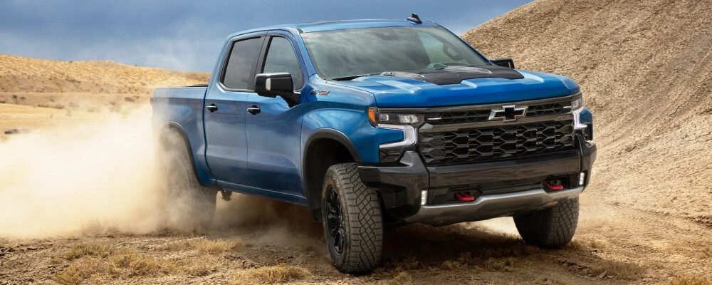 Blue Chevrolet Silverado off-road pickup truck driving through desert terrain kicking up dust
