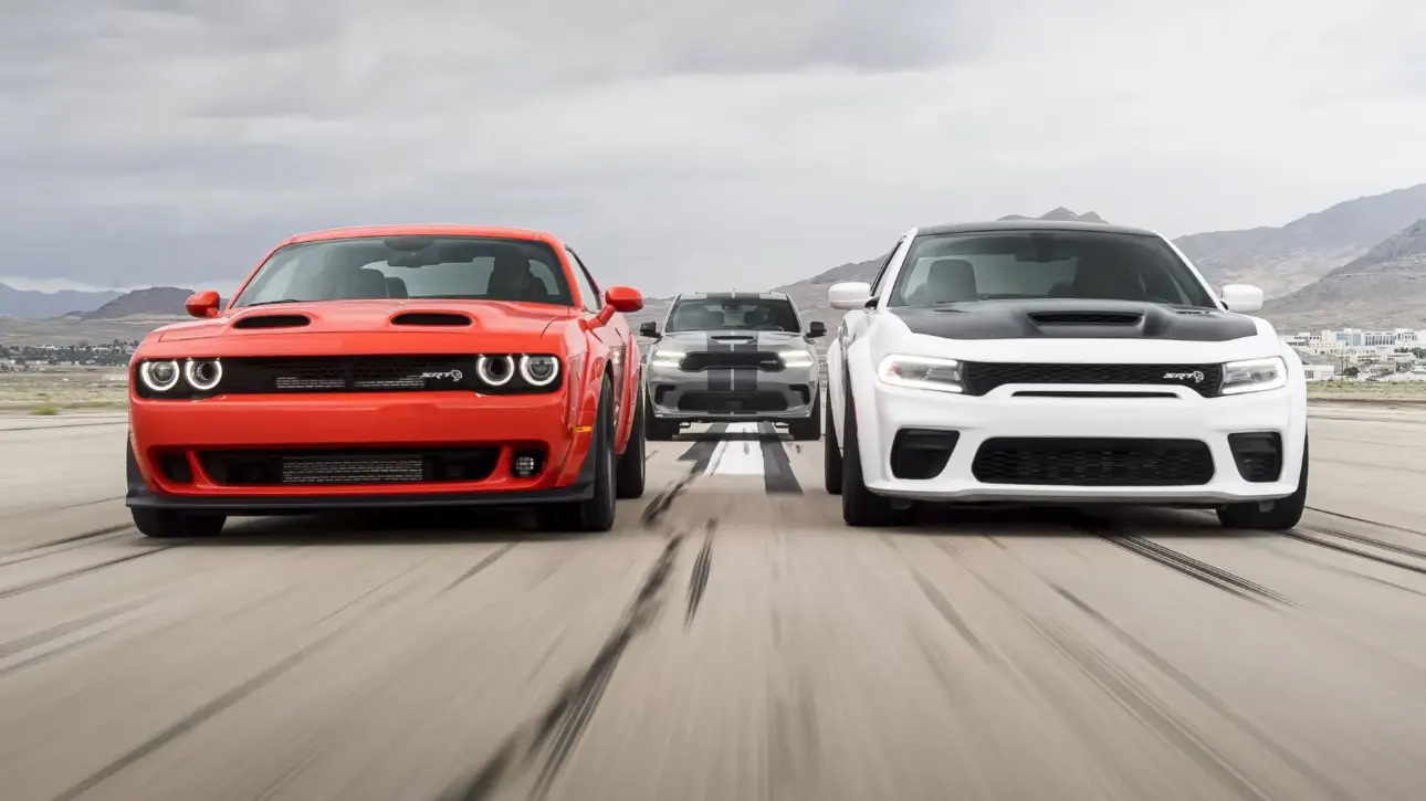 Red Dodge Challenger and white Dodge Charger muscle cars racing side by side on racetrack