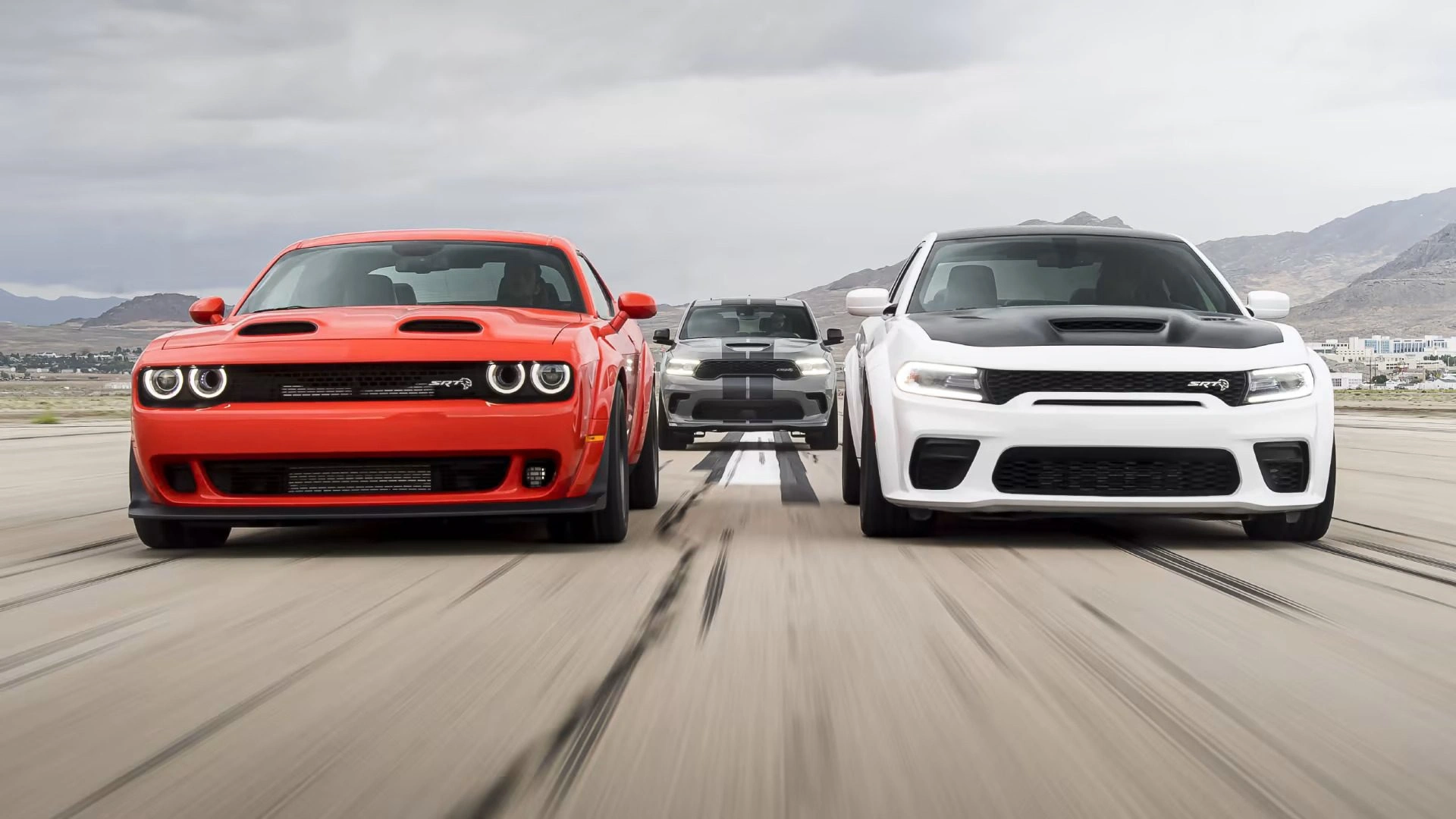 Red Dodge Challenger and white Dodge Charger muscle cars racing side by side on racetrack