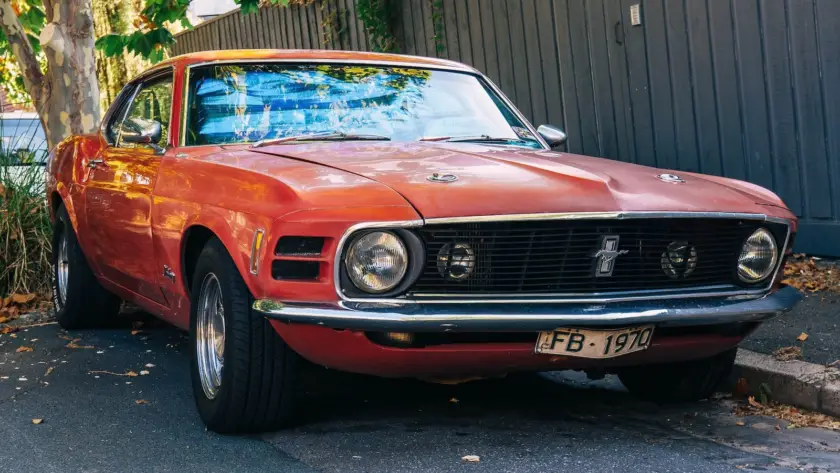 Classic orange red Ford Mustang vintage muscle car parked in front of gray corrugated metal building