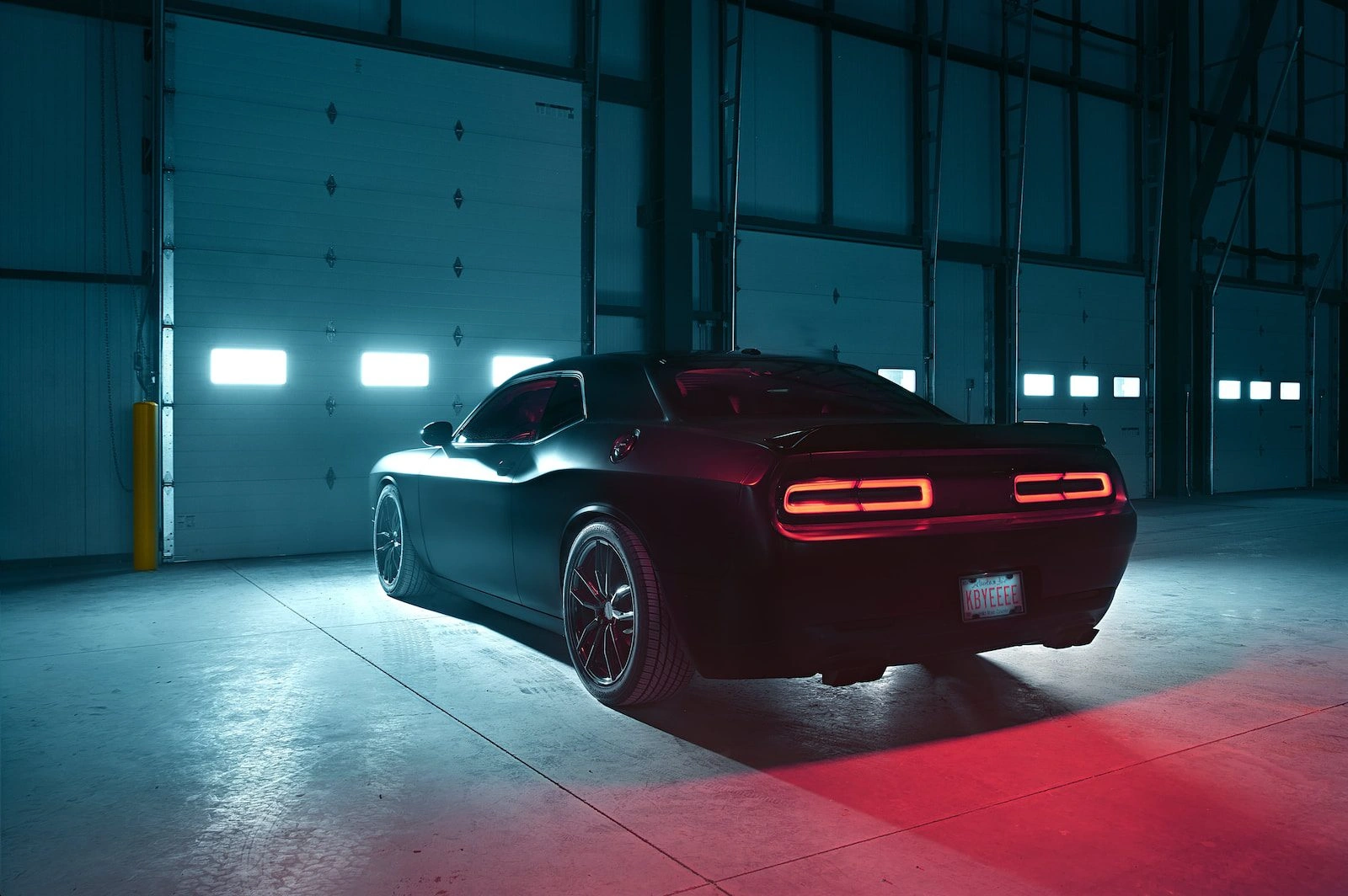 Black Dodge Challenger muscle car rear view with glowing red LED taillights in dark parking garage