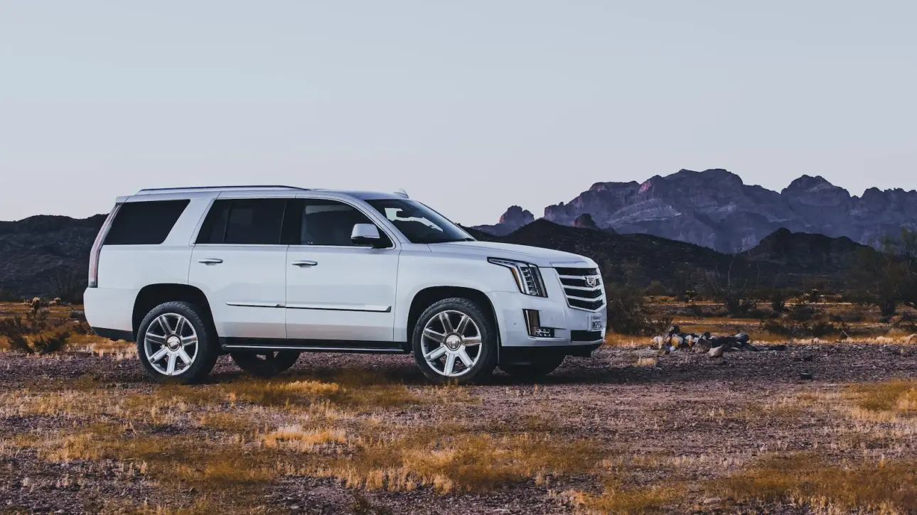 White Cadillac Escalade luxury SUV in desert landscape with mountains at sunset