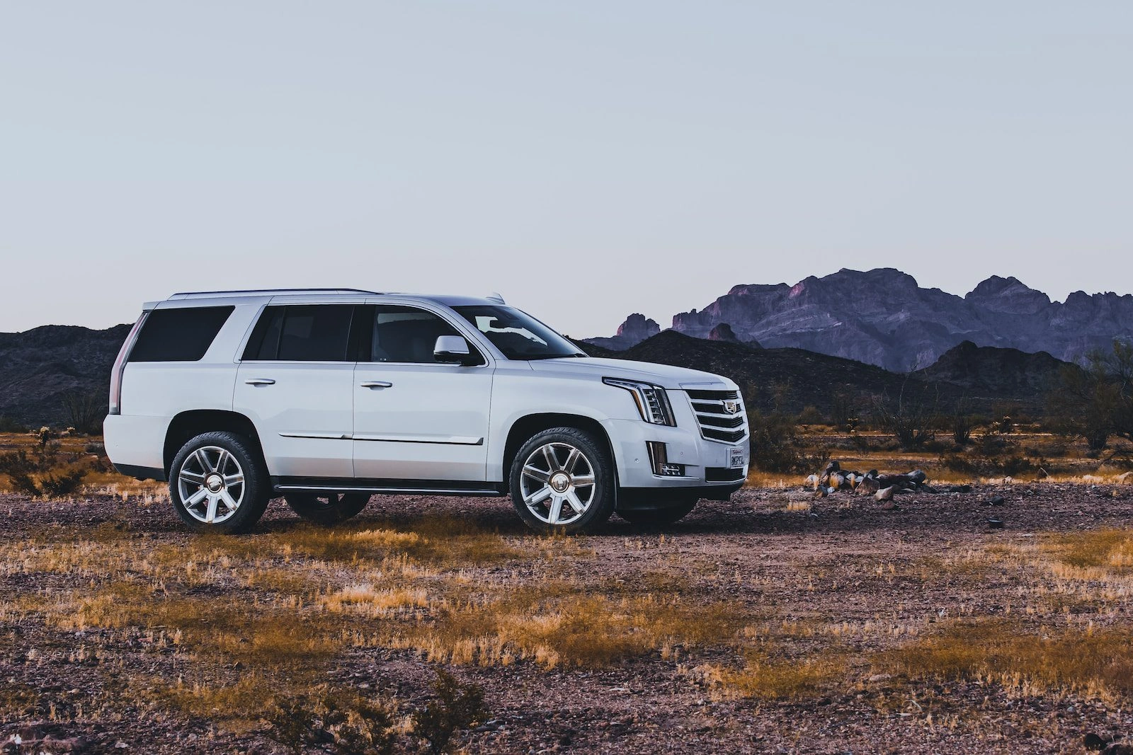White Cadillac Escalade luxury SUV in desert landscape with mountains at sunset