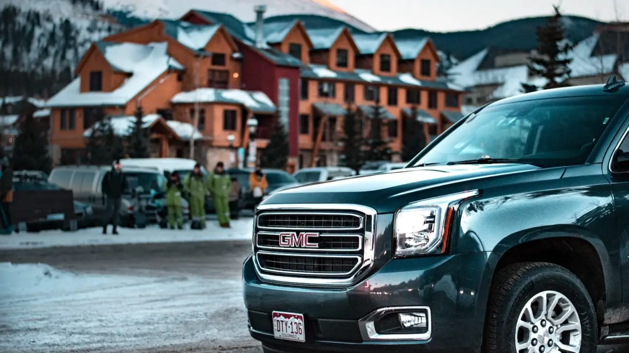 Dark blue GMC Yukon luxury SUV parked at mountain ski resort with snow-covered wooden lodge building