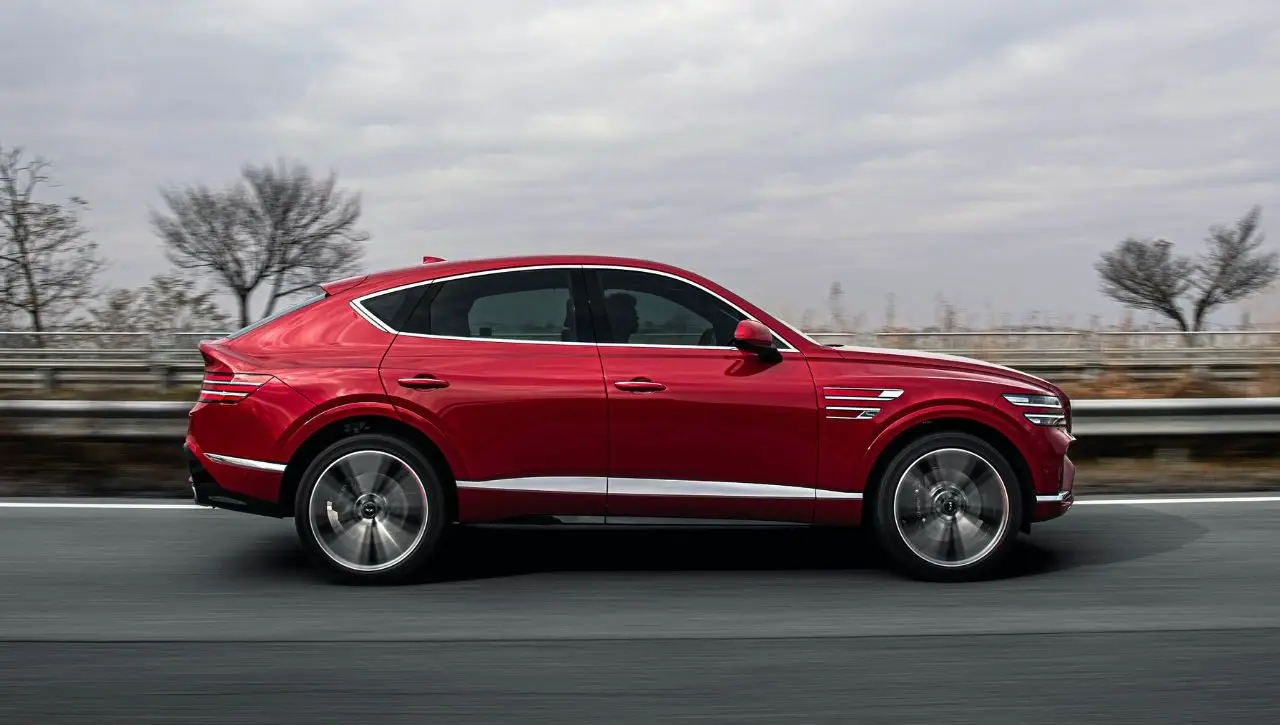 Red Genesis G80 luxury sedan driving on highway with landscape scenery in background