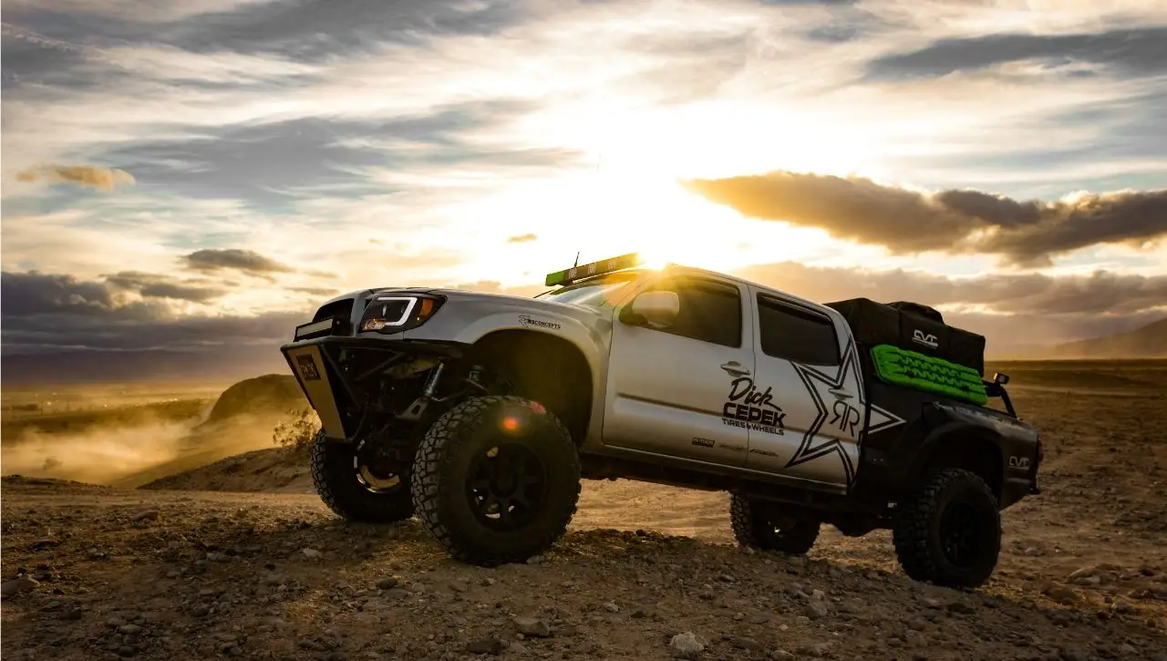 Modified white and black pickup truck with lifted suspension driving on desert terrain at sunset