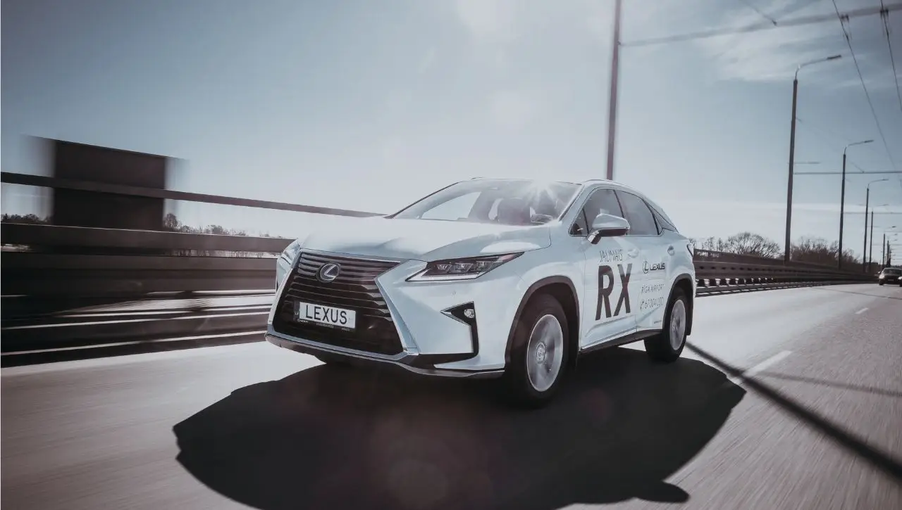 White Lexus LX600 luxury SUV driving on suspension bridge with power lines and industrial setting
