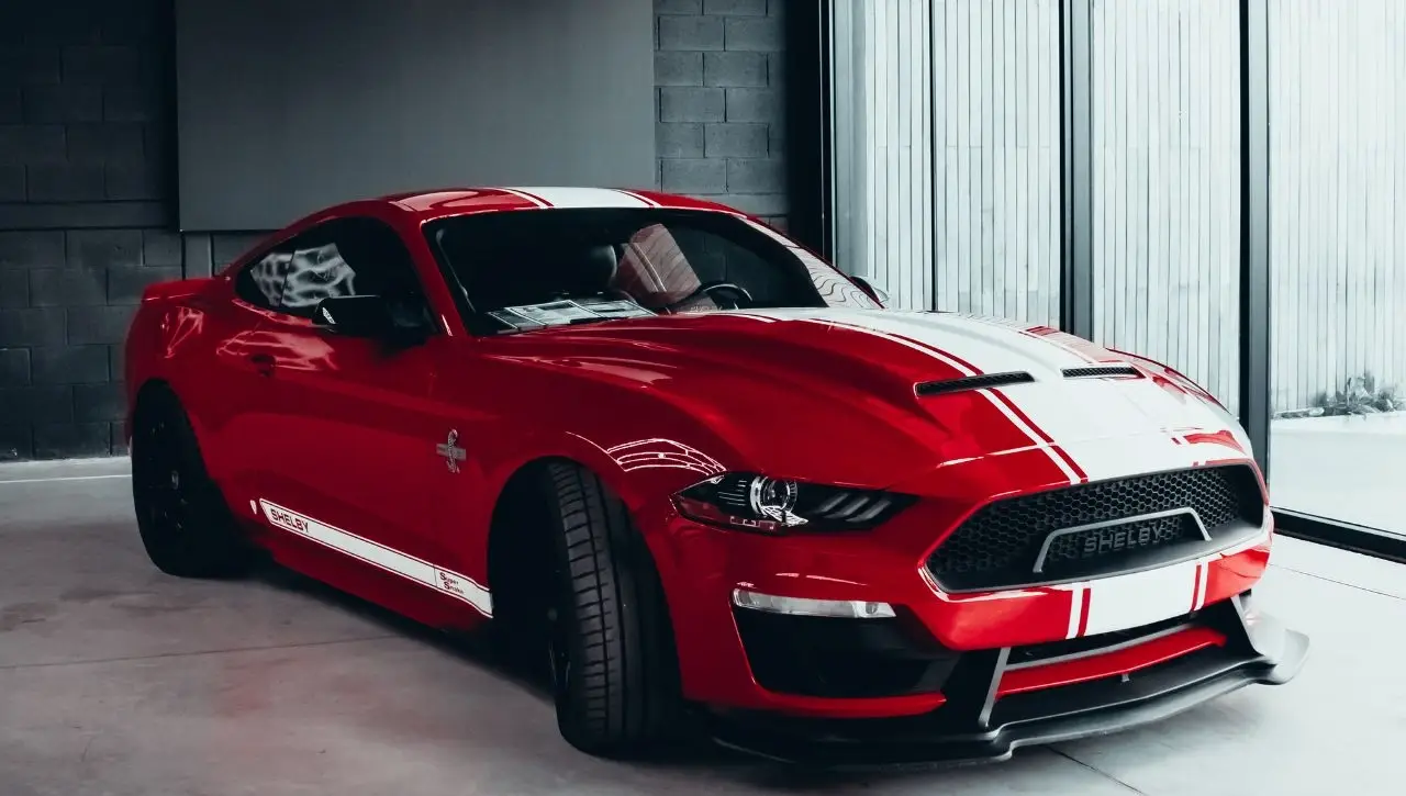 Red and white Ford Shelby Mustang sports car with racing stripes parked in modern garage setting