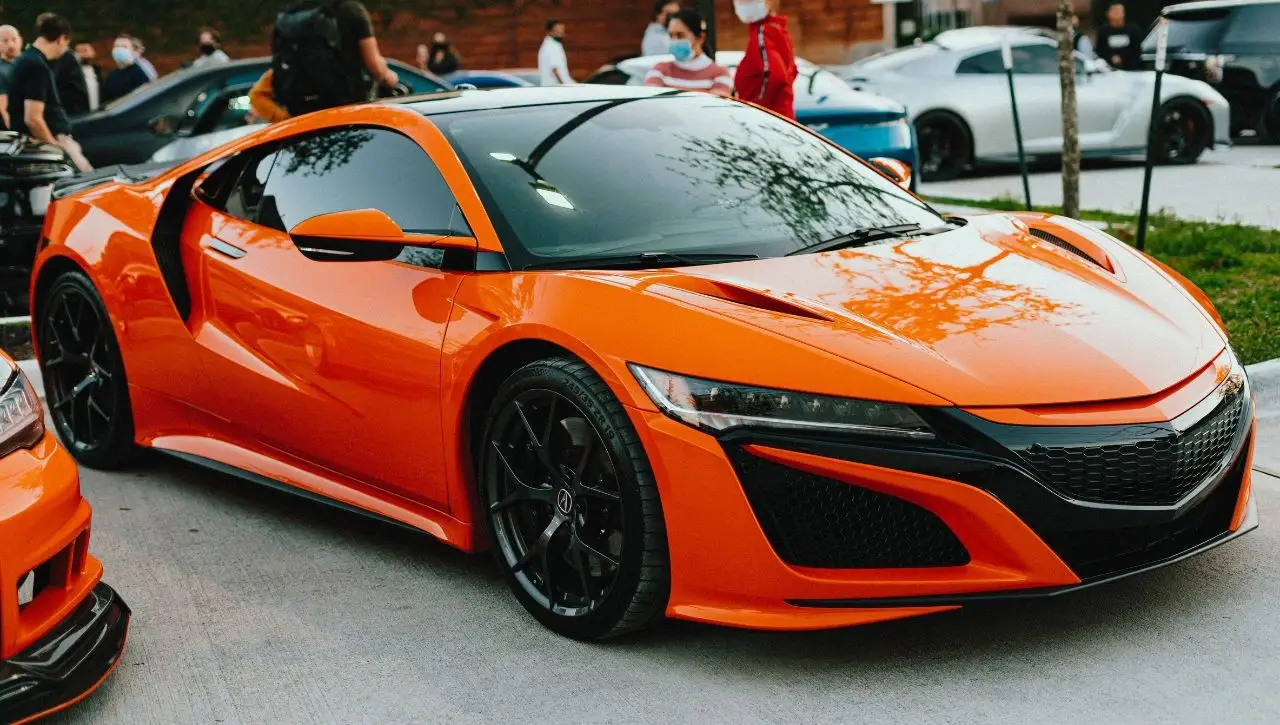Bright orange Acura NSX sports car displayed at outdoor car show event with people in background