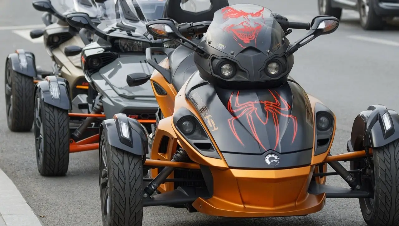 Row of customized Can-Am Ryker three-wheeled vehicles with orange and black spider web graphics parked in line