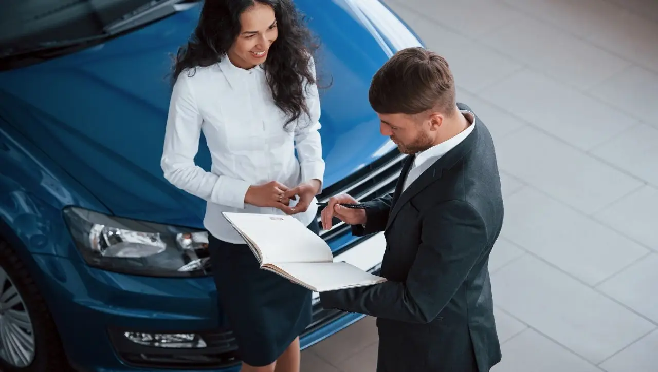 Professional couple reviewing import duties documents beside blue luxury car full cost breakdown for Indian buyers