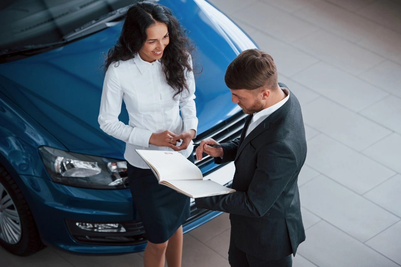 Professional couple reviewing import duties documents beside blue luxury car full cost breakdown for Indian buyers